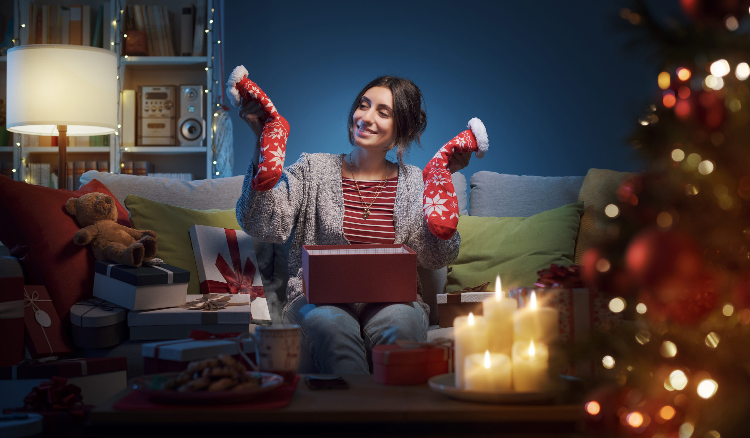 Žensa sedí na gauči a drží v ruke ponožky - vianočné darčeky.