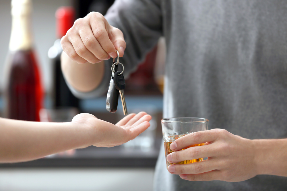 Pohľad na muža s pohárikom whisky, ktorý odovzdáva kľúče od auta; alkohol za volant nepatrí.