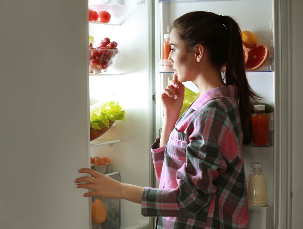 Žena stojí pri chladničke a premýšľa nad tým, čo by zjedla.