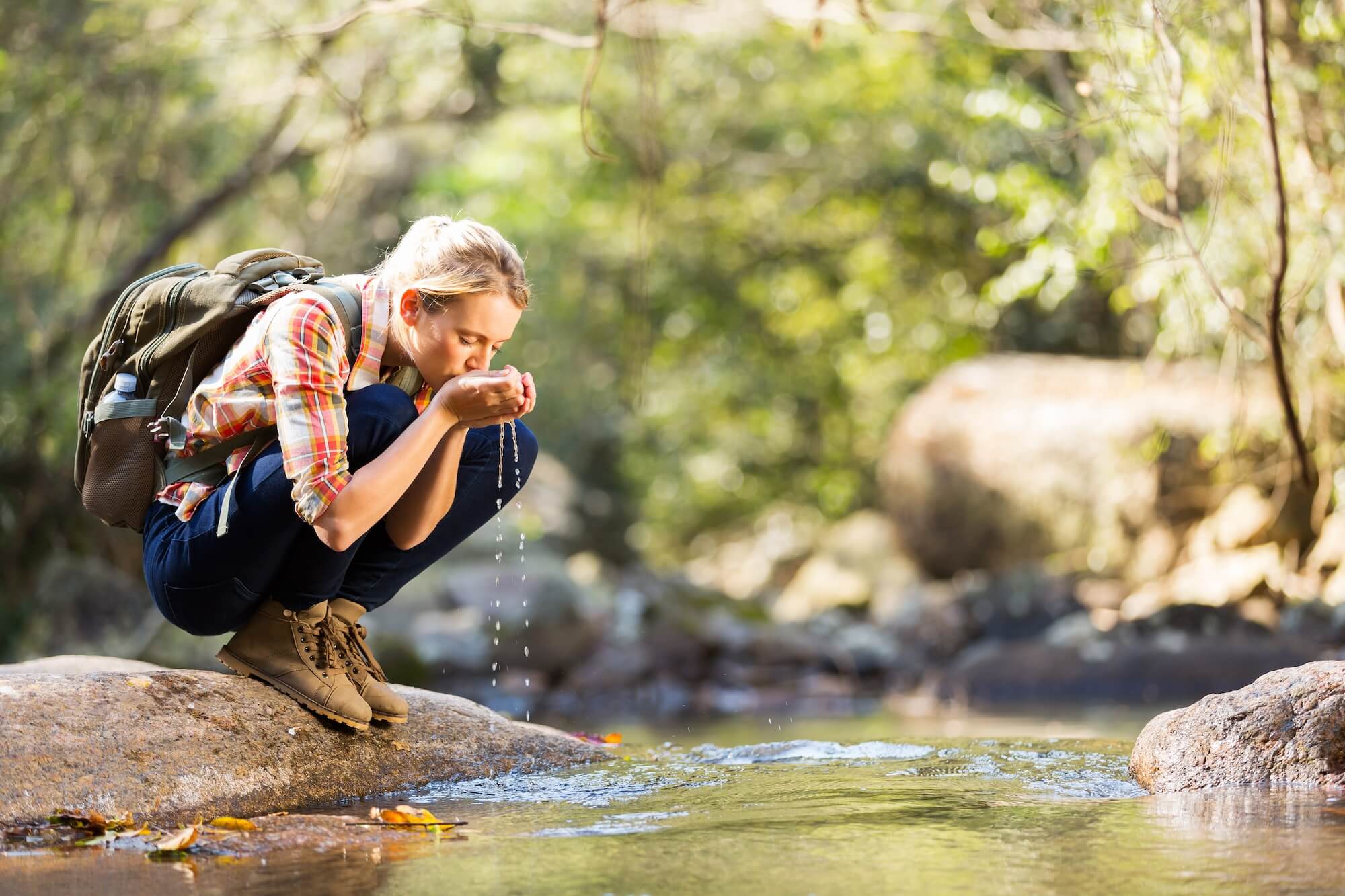 žena pije vodu z potoka