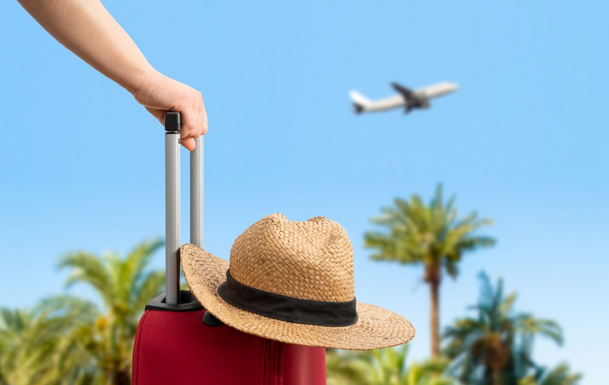 Kufor s klobúkom, v pozadí lietadlo. Cunaplus_M.Faba/iStock